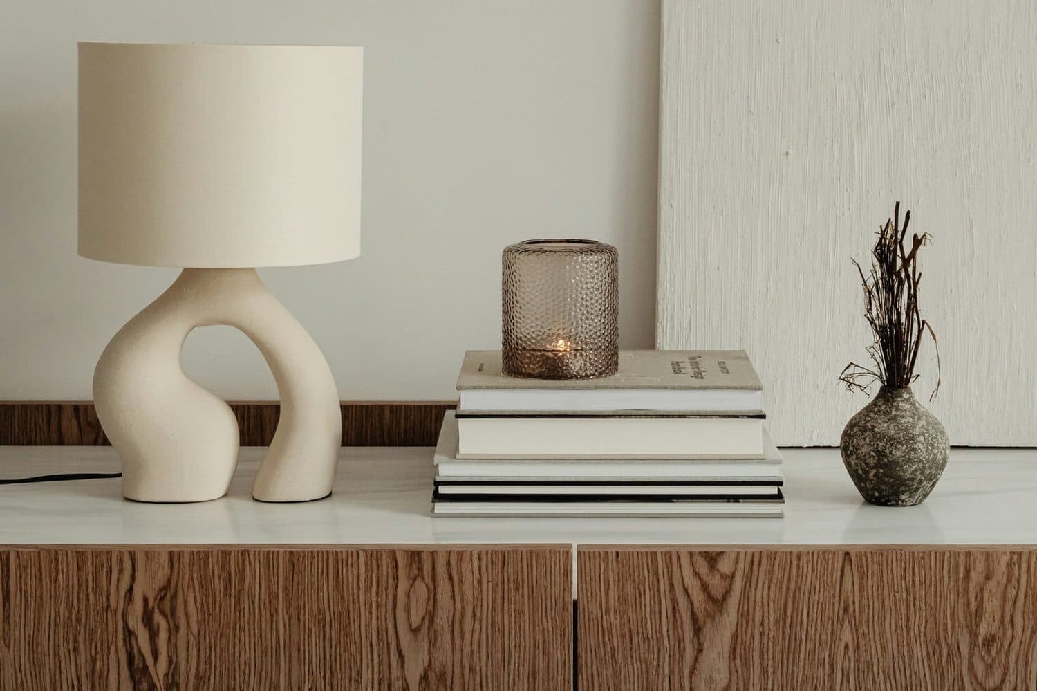 A sideboard with a ceramic lamp, books and a small vase