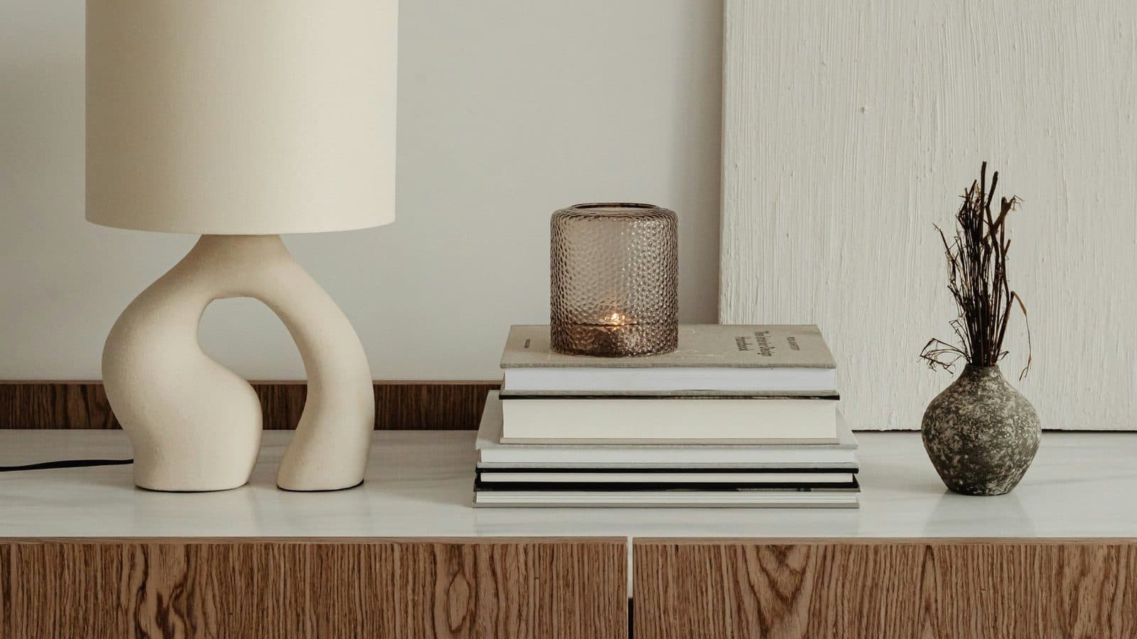 A wooden sideboard with a lamp, a stack of books and a vase
